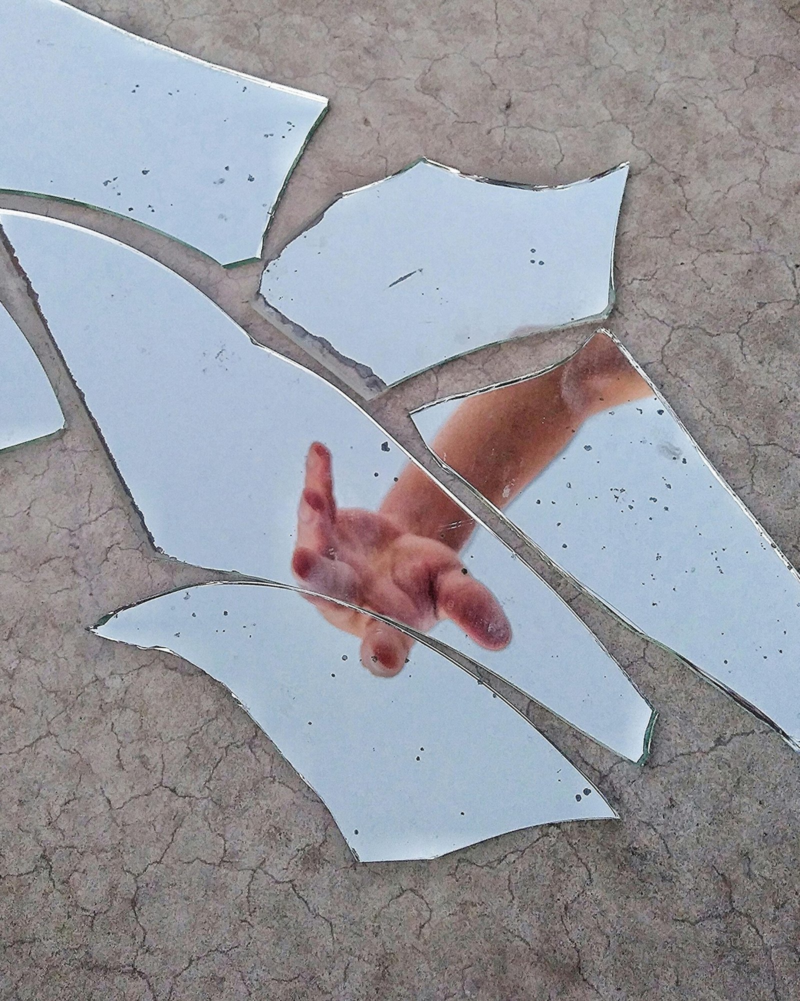 Hand reaching through broken mirror pieces on cracked ground, symbolizing healing from brokenness, self-reflection, resilience, and rebuilding life after change.